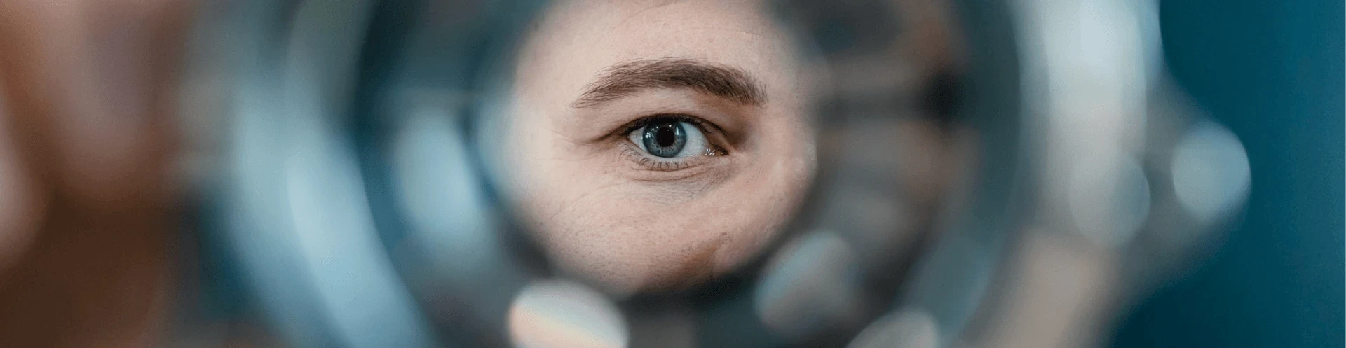 A blue eye viewed through a circular magnifier.