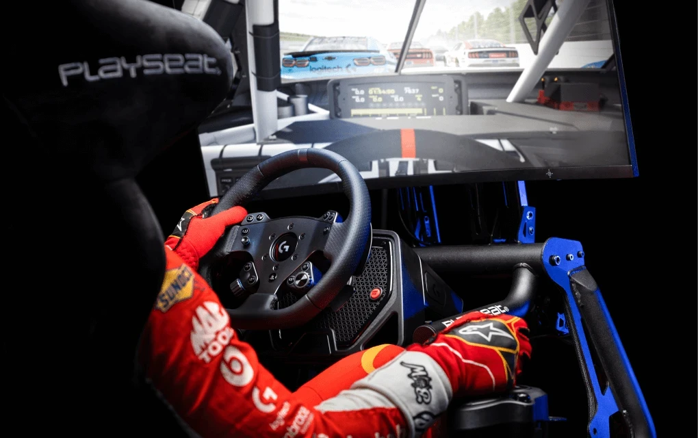 A driver in a racing uniform plays a racing simulation using a Playseat gaming chair and the Logitech G PRO Wheel and Pedals.