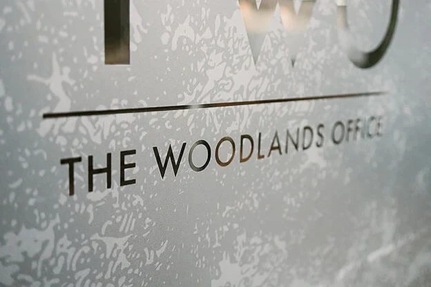A close-up view of the frosted glass wall in Adcetera’s lobby, etched with the words “TWO: The Woodlands Office.”
