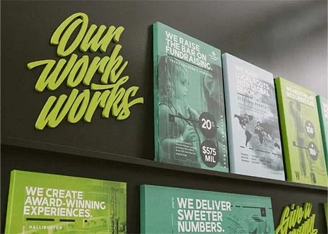 Work samples are displayed on the wall in Adcetera’s Midtown office in Houston, Texas. A sign on the wall reads, “Our Work Works.”