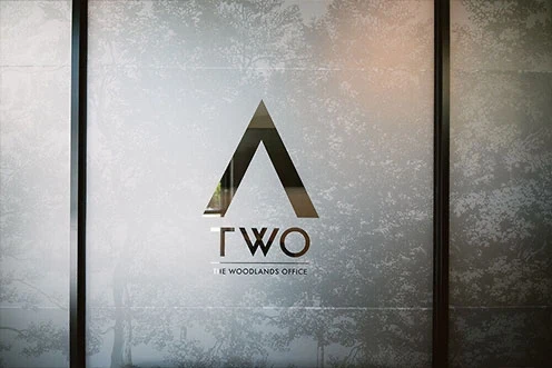 A frosted glass wall separates the lobby from the main office space. Below the Adcetera logo are the initials “TWO,” then the words, “The Woodlands Office.”