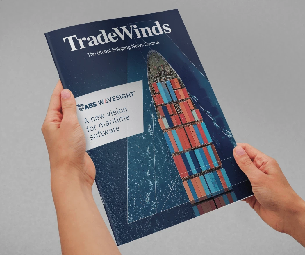Hands holding an issue of “TradeWinds” magazine with ABS Wavesight featured on the cover, including an image of a cargo ship and the headline, “A new vision for maritime software.”